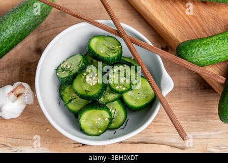 Sunomono, salade japonaise de concombre. Concombres tranchés avec vinaigrette asiatique de sauce soja, vinaigre de riz, huile de sésame, sucre et aneth dans un bol blanc sur bois ta Banque D'Images