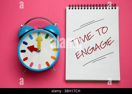 Temps d'engager la phrase écrite dans le cahier et réveil sur fond rose, vue de dessus Banque D'Images
