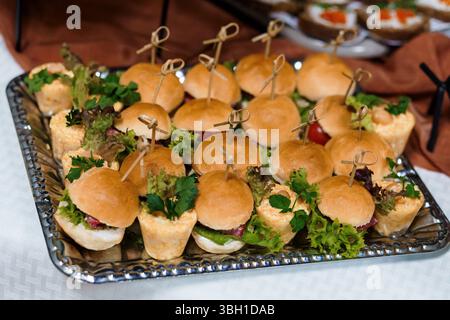 Un gros plan présente un plateau argenté rempli de sandwichs miniatures, garni de brins de persil, idéal pour la restauration, les fêtes ou les hors-d'œuvre Banque D'Images