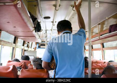 Un conducteur d'autobus interagit avec des passagers assis pendant un trajet très fréquenté dans un environnement urbain. Banque D'Images