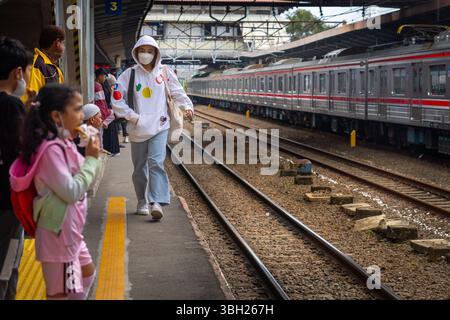 Jakarta, Indonésie - 9 février 2025 : une femme portant un sweat à capuche blanc marche sur la voie ferrée. Une fille dans un sweat à capuche rose est debout sur la plate-forme à Banque D'Images