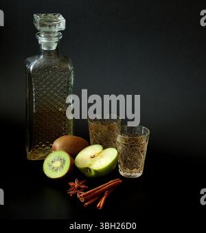 Liqueur de fruits à base de kiwi et pomme verte avec cannelle et anis dans un verre de cristal sur fond noir. Gros plan. Banque D'Images