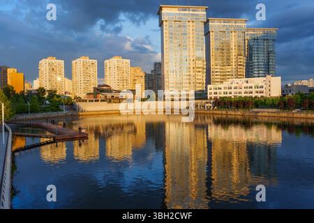 Kiev, Ukraine - 19 mai 2025 : vue sur les gratte-ciel modernes de Kiev reflétant sur l'eau calme pendant le coucher du soleil, avec un éclairage chaleureux et une atmosphère sereine Banque D'Images