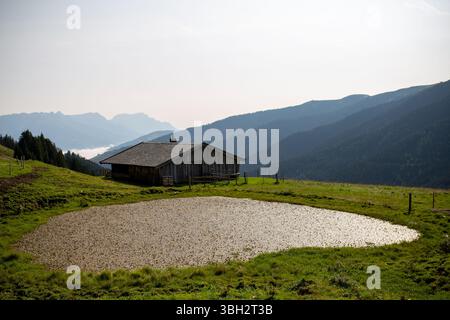 Une cabane traditionnelle en bois avec un toit sombre se dresse sur une pente herbeuse, accompagnée d'un petit étang ou d'un lac artificiel Banque D'Images