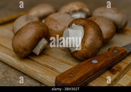 Image en gros plan de champignons cremini frais disposés sur une planche à découper en bois avec un couteau. Banque D'Images