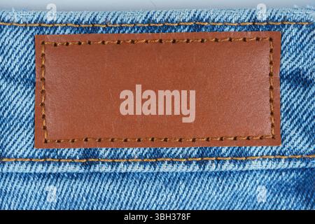 Gros plan de l'étiquette en cuir marron cousue sur un Jean denim bleu. Macro texture du tissu et des coutures. Idéal pour la mode, le textile ou les concepts de marque dans la publicité Banque D'Images