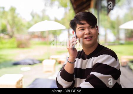 Jeune homme gay mignon assis à l'extérieur dans le restaurant café pendant la journée Banque D'Images