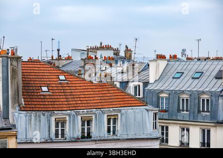 Toits de Paris en décembre avec tuiles classiques en zinc et terre cuite, cheminées, antennes et vue lointaine sur la Tour Eiffel sous un ciel nuageux Banque D'Images