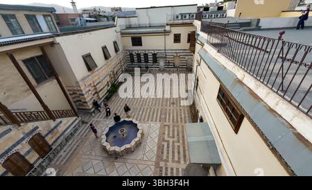 Vue aérienne d'une cour historique avec sol en pierre à motifs, entourée de bâtiments anciens. Les gens sont rassemblés autour d'une fontaine centrale. A Dama Banque D'Images