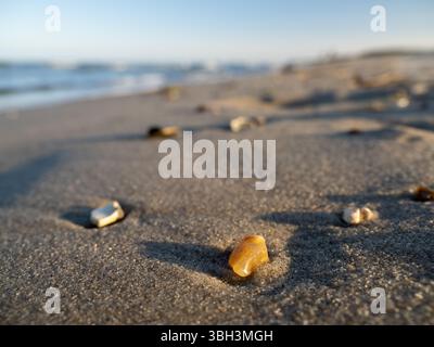 Pierre jaune sur une plage de sable dans le soleil du soir projetant une longue ombre avec la mer en arrière-plan Banque D'Images