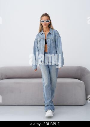 Le modèle blond présente une tenue en denim élégante dans un cadre studio moderne Banque D'Images