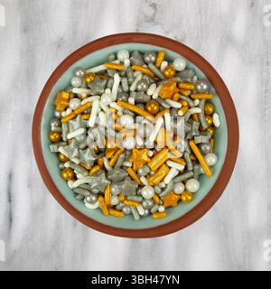 Vue de dessus d'un petit bol rempli de pépites festives sur le thème des fêtes sur un comptoir en marbre gris. Banque D'Images