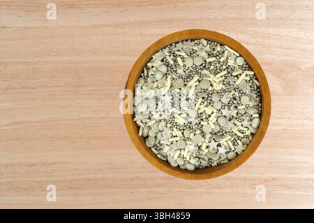 Vue de dessus de pépites festives argentées et blanches dans des formes assorties dans un petit bol sur un comptoir en bois. Banque D'Images