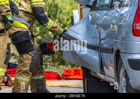 Trois pompiers ont ouvert une voiture après un accident lors d'une opération de sauvetage pour tirer le conducteur, qui est pris au piège et inconscient, hors de la voiture. Banque D'Images