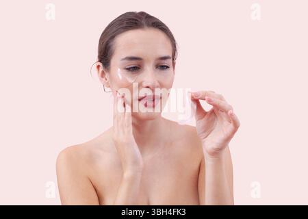 Portrait d'une jeune femme avec un look de maquillage naturel, en appliquant du silicone sous les patchs oculaires. Concept de soin de la peau pour cernes noirs, isolé sur fond rose Banque D'Images