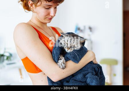 chat domestique mouillé lavé pelucheux enveloppé dans une serviette dans les bras de la jeune femme Banque D'Images