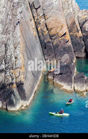 Kayak autour de la côte à Porthclais avec des grimpeurs sur les falaises, Pembrokeshire, pays de Galles, Royaume-Uni Banque D'Images