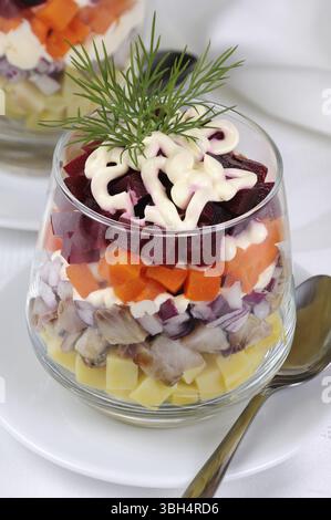 Salade de hareng haché avec les oignons, les pommes de terre, betteraves, carottes, assaisonné de sauce au yogourt dans un verre Banque D'Images