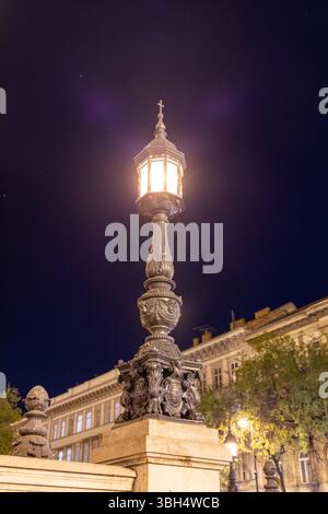 Un lampadaire de style ancien magnifiquement détaillé brille chaleureusement dans un ciel nocturne clair, jetant la lumière sur l'architecture classique de Buil environnant Banque D'Images