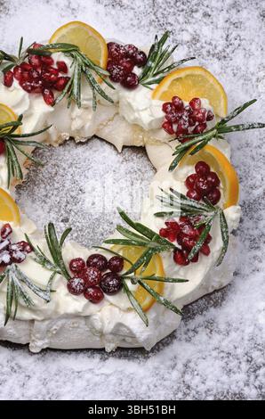 Pavlova gâteau à la forme d'une couronne de Noël de meringue avec crème, grenade, canneberge, brins de romarin Banque D'Images