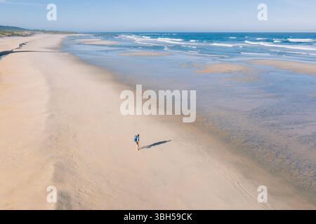 Vue aérienne de la femme marchant le long de la large plage de sable et profitant des vagues de l'océan Atlantique au Portugal. Tourné pendant le Camino Portugais — populaire Banque D'Images