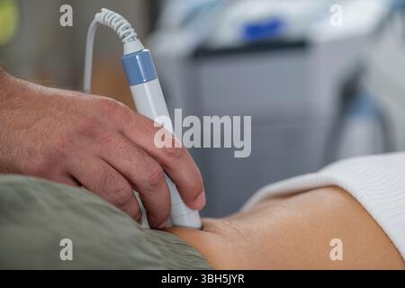 Physiothérapeute utilise la thérapie au laser sur un patient dans le bas du dos pour soulager la douleur, réduire l'inflammation et favoriser la guérison des tissus, améliorant la mobilité et la récupération. Banque D'Images