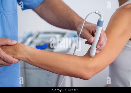 Physiothérapeute utilise la thérapie au laser sur le coude d'un patient pour soulager la douleur et accélérer la guérison. Le traitement au laser cible les tissus mous pour réduire l'inflammation et favoriser la récupération. Banque D'Images