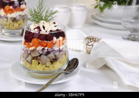 Salade de hareng haché avec les oignons, les pommes de terre, betteraves, carottes, assaisonné de sauce au yogourt dans un verre Banque D'Images