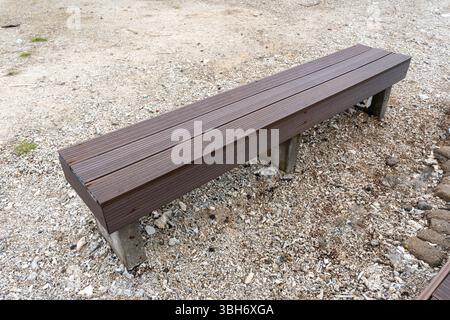 Banc en bois est assis sur une surface de gravier. Le banc est long et a une couleur marron Banque D'Images