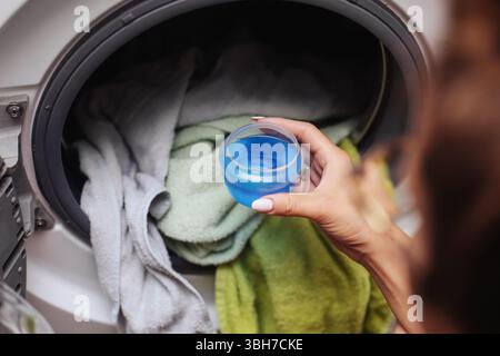 Assouplissant liquide verseur pour tissus. Tenir le capuchon avec conditionneur bleu près de la machine à laver. Produit d'entretien du linge pour la douceur et le parfum. Banque D'Images