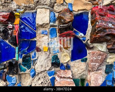 Mosaïque brillante de fragments de verre colorés encastrés dans un mur de pierre. L'image symbolise la créativité urbaine et les détails architecturaux Banque D'Images