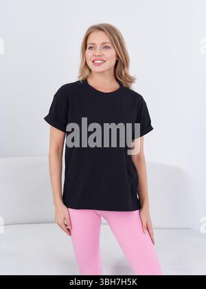 Individu souriant dans un t-shirt noir et un pantalon rose se tient en toute confiance, dégageant un style décontracté et une énergie positive. Les cheveux courts ajoutent au look Banque D'Images