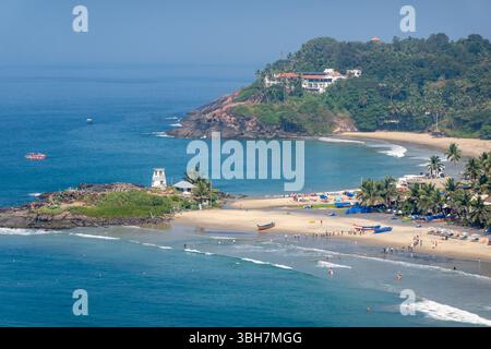Plage tropicale au Kerala, Inde, avec des bateaux de pêche, des palmiers, et des touristes appréciant l'océan sous un ciel bleu Banque D'Images