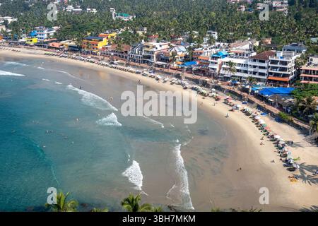 Vue de dessus de Lighthouse Beach à Kovalam, Kerala, Inde, bordée de parasols colorés, de bâtiments en bord de mer et de gens appréciant l'océan et le rivage sablonneux Banque D'Images