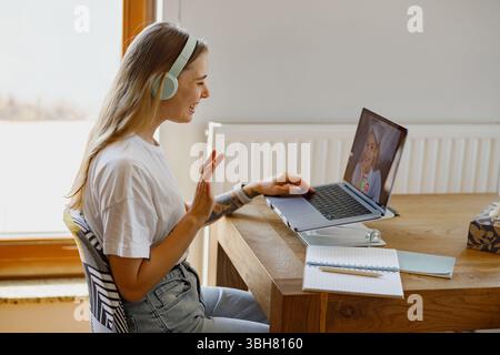 Une jeune femme se lançant volontiers dans un appel vidéo tout en travaillant depuis son bureau à domicile confortable Banque D'Images