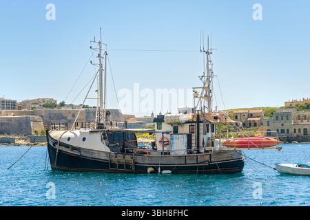 Vieux bateau de pêche en bois ancré dans des eaux bleues calmes, avec de hauts mâts, des bouées de sauvetage et des détails rustiques. Bâtiments côtiers et fortifications Banque D'Images