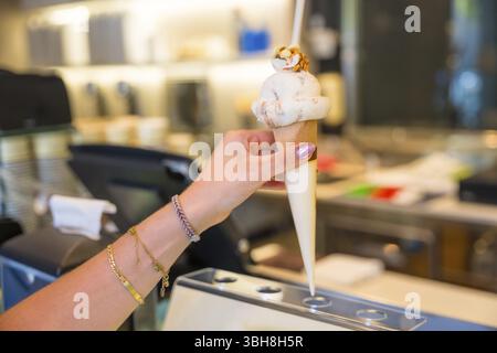 Femmes à la main orné de bracelets, tenant un délicieux cône de crème glacée surmonté de noix croquantes, appréciant une friandise dans une gelateria Banque D'Images