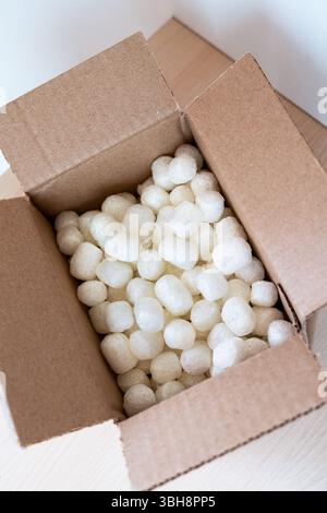 Boîte en carton ouverte remplie d'arachides d'emballage écologiques à base de maïs sur une surface en bois clair. Emballage durable pour shippin sûr et conscient Banque D'Images