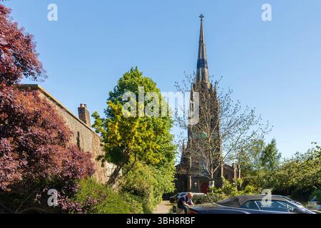Londres, Royaume-Uni, le 5 mai 2025, Une église historique avec une flèche proéminente se dresse derrière une rangée d'arbres et un mur de briques, avec une voiture garée dans le Forward Banque D'Images