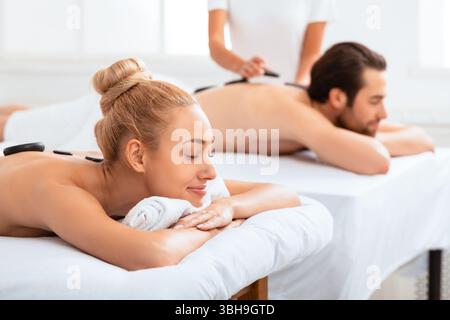 Couple recevant un massage aux pierres chaudes en profitant d'un soin de beauté à l'intérieur Banque D'Images