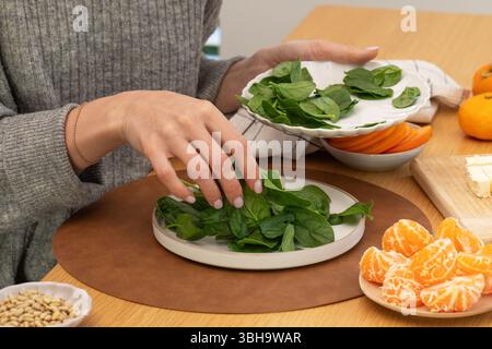 Femme mettant des épinards de bébé frais dans l'assiette à la table en bois. Préparer une salade d'épinards frais Banque D'Images