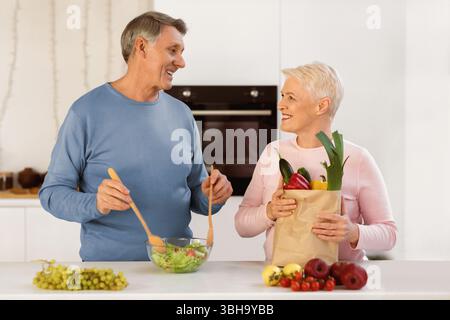 Couple âgé debout avec un forfait plein de provisions dans la cuisine Banque D'Images