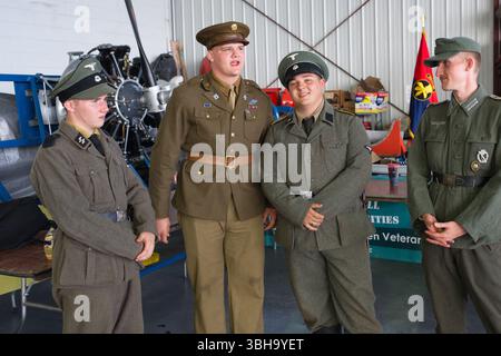 Quatre hommes en uniforme militaire se tiennent dans un hangar. Deux portent des uniformes allemands de la seconde Guerre mondiale ; un porte un uniforme de l'armée américaine ; un porte un uniforme allemand de la Luftwaffe. Banque D'Images
