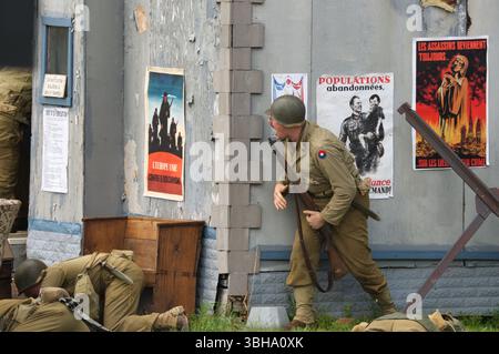 Un soldat portant un uniforme de l'armée américaine de la seconde Guerre mondiale, accroupi derrière un bâtiment, tient un fusil. L'extérieur du bâtiment est altéré, et plusieurs propag Banque D'Images