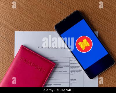Un passeport, un formulaire de demande de visa et un smartphone affichant le drapeau ASEAN sur une table en bois. Concept de voyage international et de connexions mondiales Banque D'Images