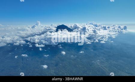 Les nuages tourbillonnent autour du pic volcanique, révélant les pentes escarpées et les riches forêts verdoyantes. La scène capture la beauté sauvage de cette île tropicale Banque D'Images
