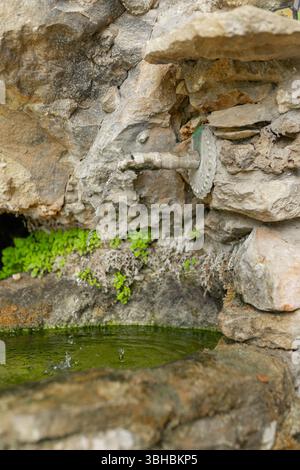 Fontaine rustique en pierre altérée avec tuyau d'égouttement et bassin d'eau. Banque D'Images