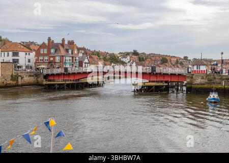 Whitby Swing Bridge enjambant la rivière Esk, sa ferronnerie peinte traversant l'eau, avec des bâtiments au bord du port et la vieille ville derrière. Banque D'Images
