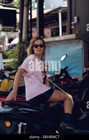 Femme en chemise rose monter sur scooter, tenant les clés Banque D'Images