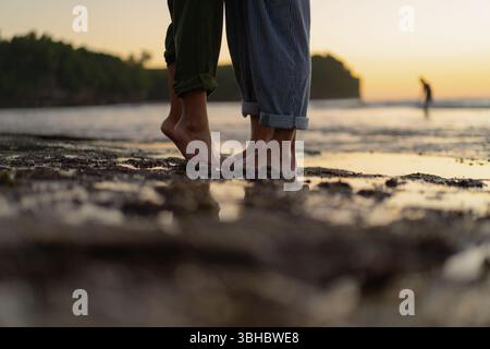 Couple pieds nus debout près les uns des autres sur la plage au coucher du soleil Banque D'Images